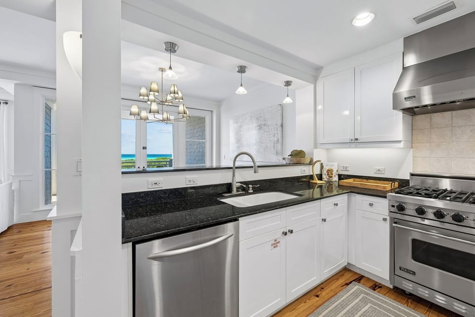 This stunning kitchen features sleek stainless appliances, gorgeous granite countertops, and crisp white cabinetry. Through the window, catch glimpses of sparkling ocean views that frame your coastal culinary experience perfectly.