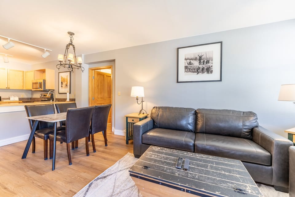 Relax in your stylish open-plan living space with plush leather seating, modern dining area, and thoughtfully curated ski lodge artwork.