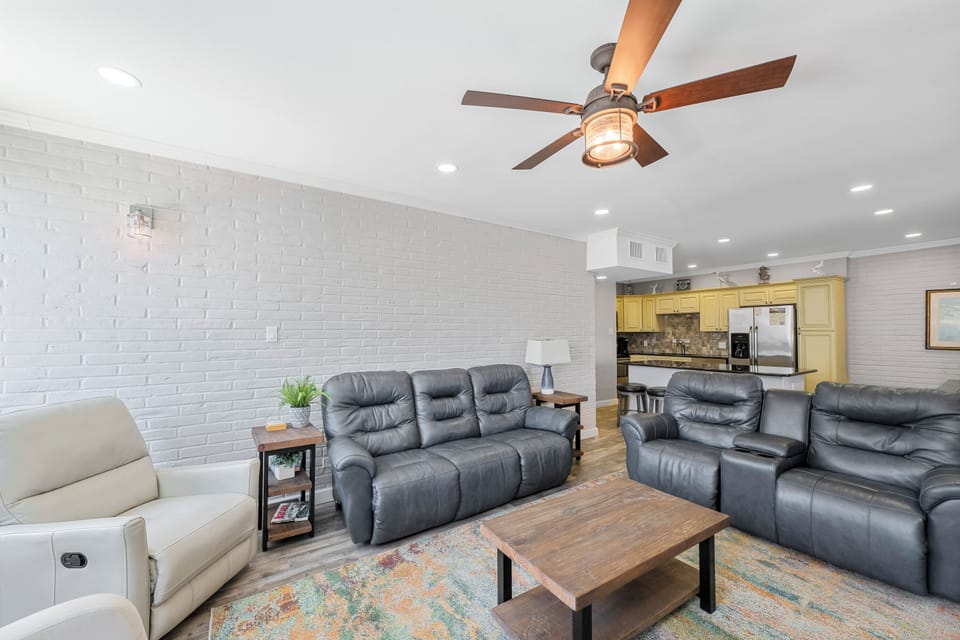 Relax in your spacious living room featuring comfortable leather recliners, modern brick accent wall, and charming ceiling fan.