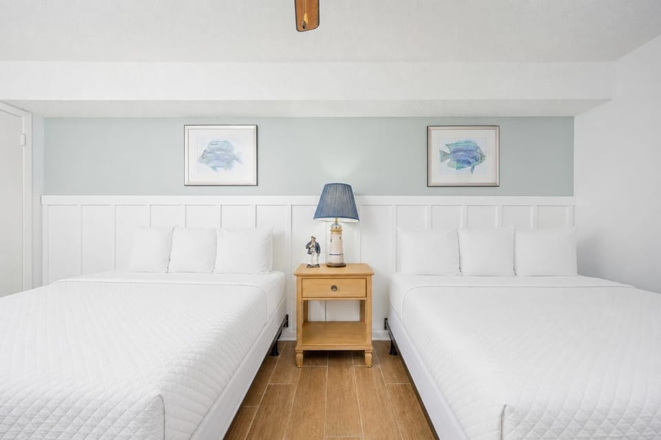 Enjoy restful nights in this inviting guest room featuring two queen beds and coastal artwork