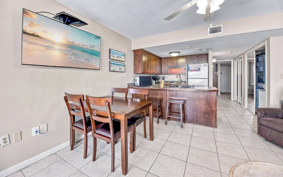 Enjoy the spacious dining area with seating for four, a large wall-mounted flat-screen TV, and two convenient barstools at the breakfast bar