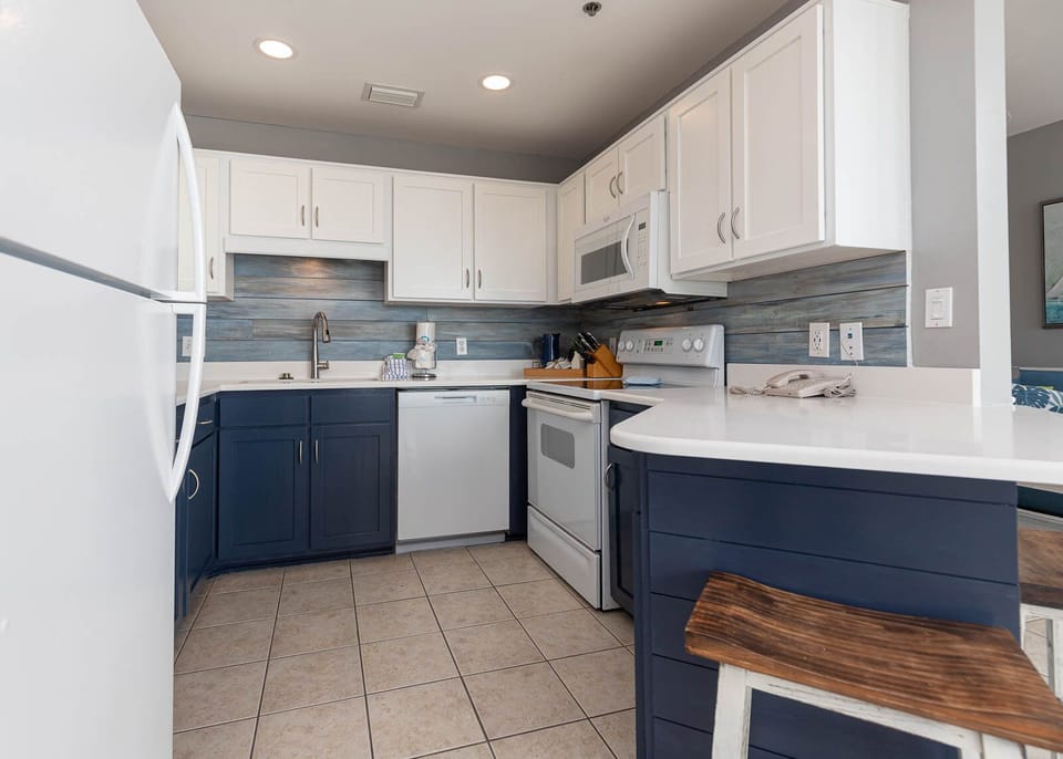 This modern kitchen features navy blue cabinetry, white countertops, and a convenient breakfast bar with seating