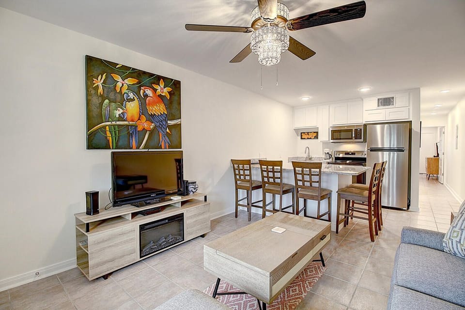 Relax in your bright, modern living space featuring a fully equipped kitchen, dining area, and entertainment center with colorful tropical artwork.