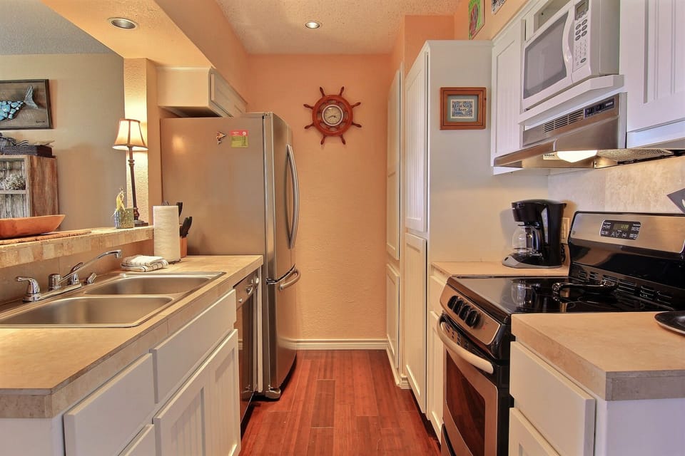 Cook your favorite meals in this well-equipped kitchen featuring stainless steel appliances, white cabinetry, and warm hardwood floors.