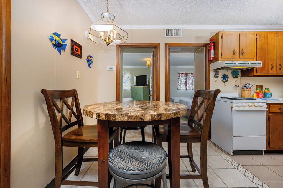 The cozy dining area features a round table with a marble top, wooden chairs, and a view into the kitchen with colorful decor