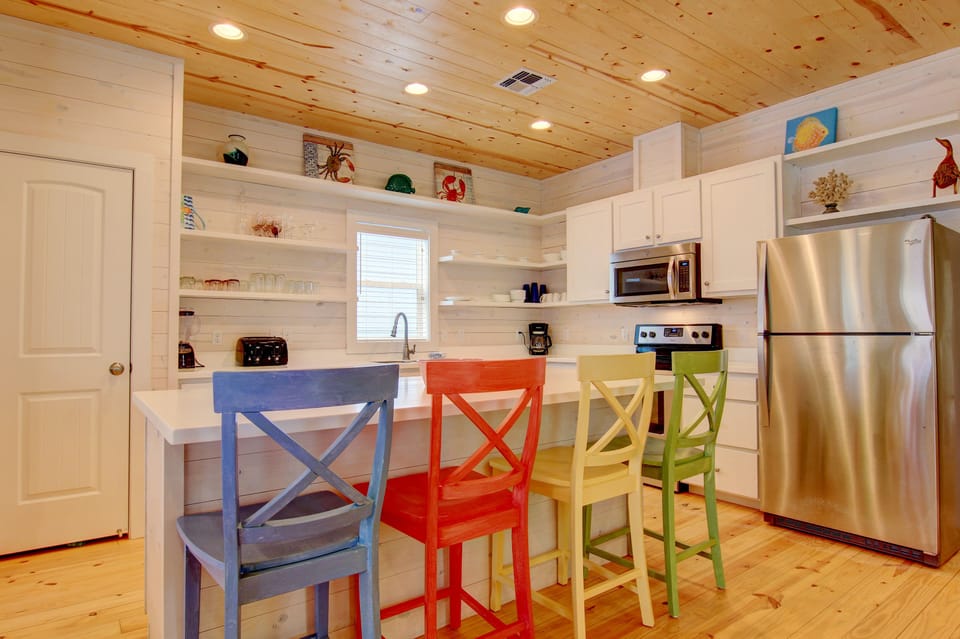 Your bright kitchen invites culinary adventures with colorful seating, open shelving, and modern appliances under charming wood ceilings.