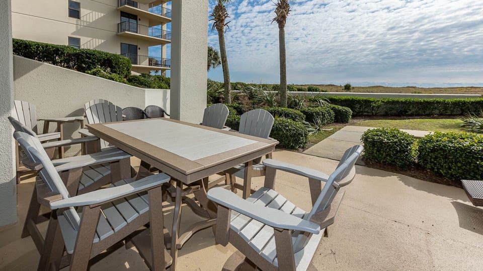 Outdoor dining area features a large table surrounded by comfortable chairs, with lush greenery and palm trees in view