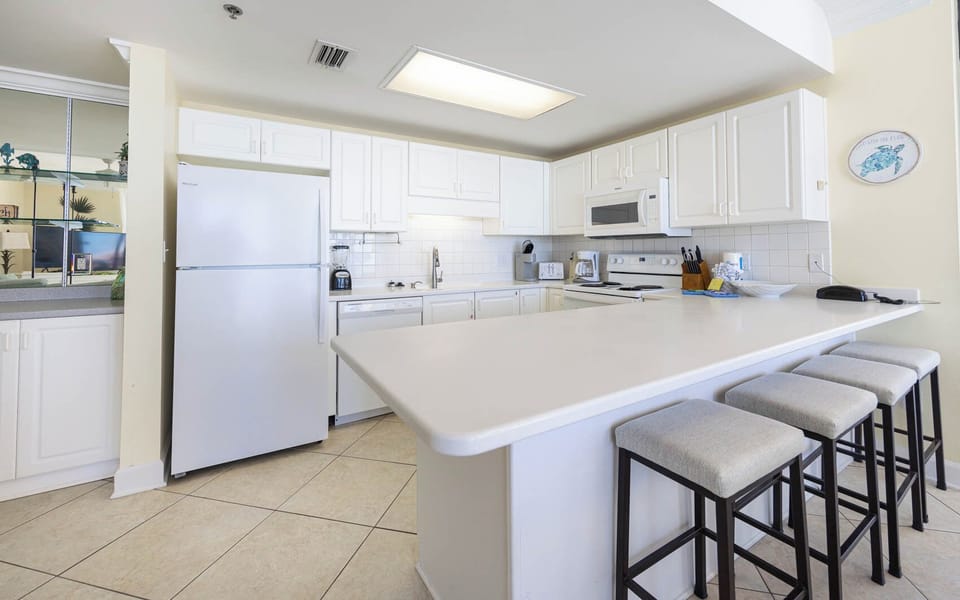 White cabinetry complements the spacious counter, featuring a breakfast bar, white appliances, and seating for four
