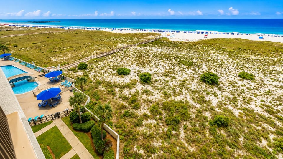 Blue umbrellas shade the poolside seating where you relax while watching the sparkling gulf water beyond the dunes