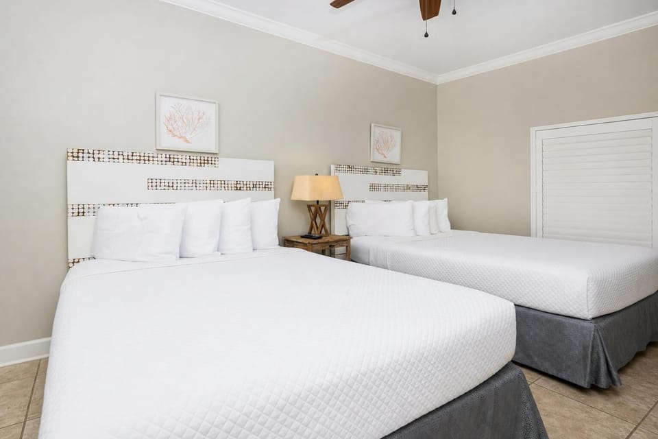Rest comfortably in this inviting guest room with two queen beds, soft decor, and warm lighting for a relaxing stay