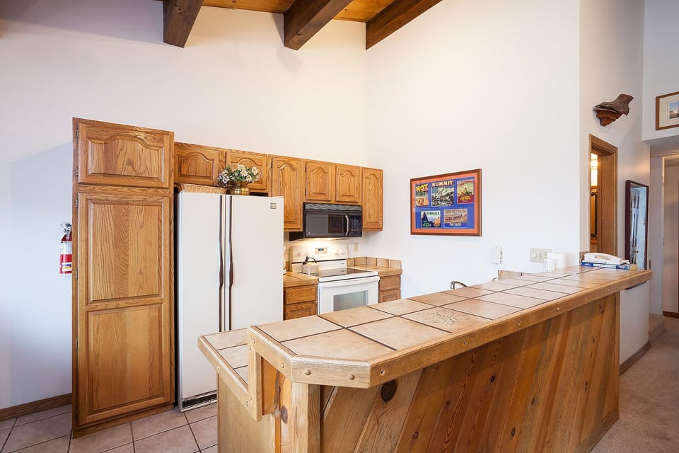 Gather around your spacious kitchen island with tiled countertops and rustic wood accents, where exposed beams create a cozy mountain retreat atmosphere.