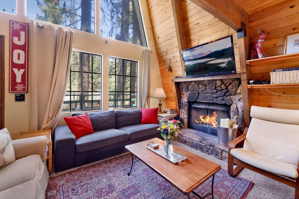 Cozy mountain living room with a stone fireplace, comfy seating, and smart TV—perfect for relaxing evenings, movie nights, and warm cabin vibes after outdoor adventures.