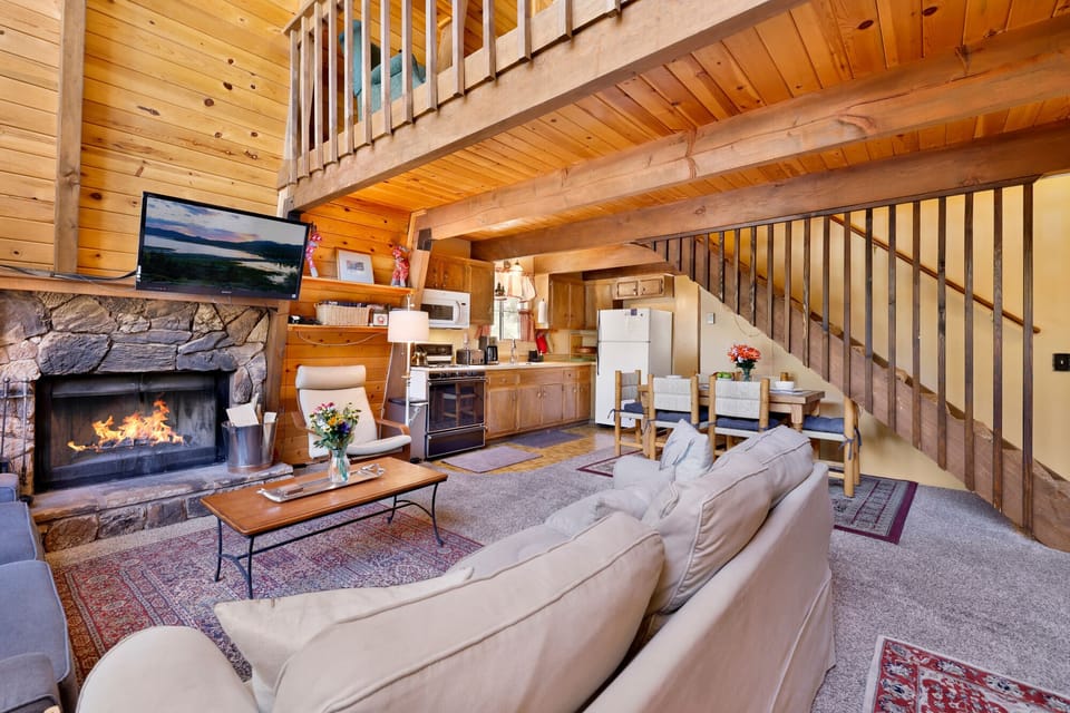 Cozy mountain living room with a stone fireplace, comfy seating, and smart TV—perfect for relaxing evenings, movie nights, and warm cabin vibes after outdoor adventures.