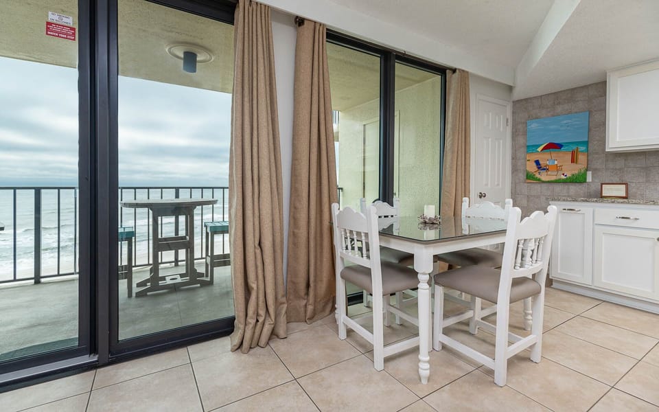 This inviting dining area features a glass-top table, white chairs, and a lovely view of the beach from the balcony