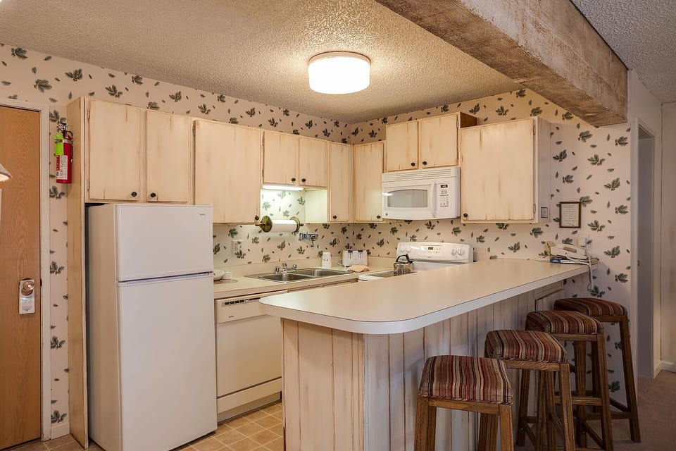 Your cozy kitchen features rustic charm with leafy wallpaper, warm wood beams, and everything you need to prepare meals during your stay.