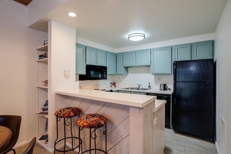 Your fully equipped kitchen features sage-green cabinets, modern appliances, and a breakfast bar where you can savor morning coffee.