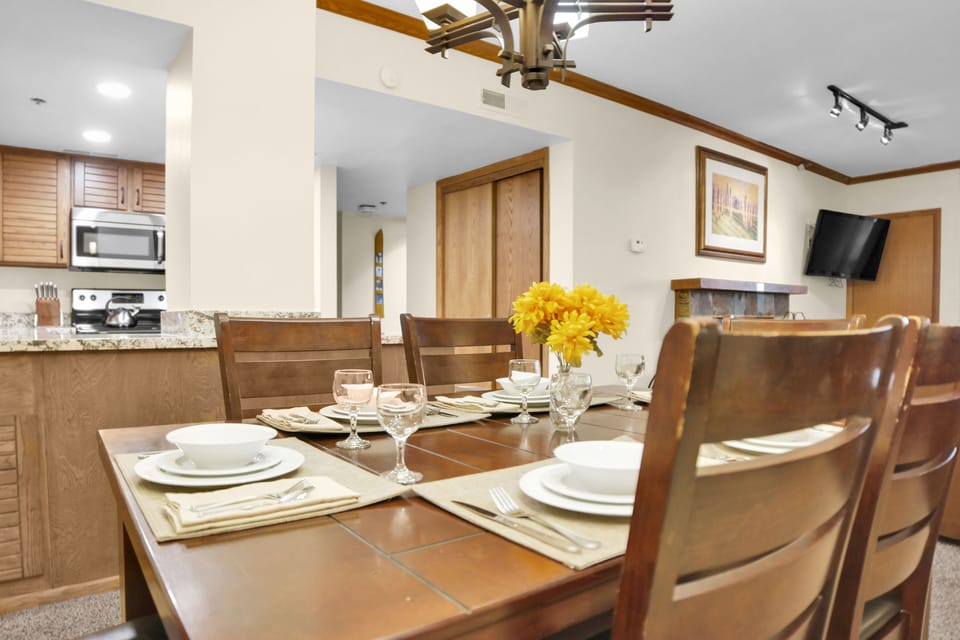 Park Station 214's dining table is set for 6 guests with white dishes, cream placemats and yellow flowers in the center.
