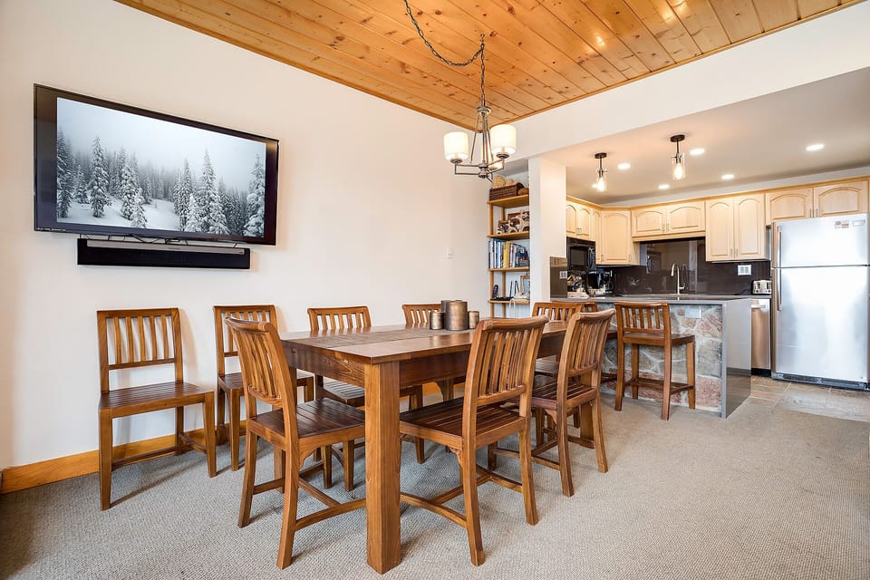 Gather around your spacious dining table for memorable meals, with a fully equipped kitchen and cozy wood ceiling creating the perfect mountain retreat atmosphere.
