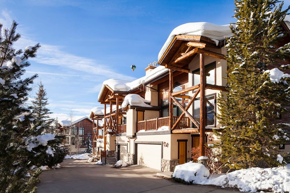 A stunning alpine chalet with snow-covered roofs nestled among evergreen trees, offering mountain luxury in a winter wonderland setting.