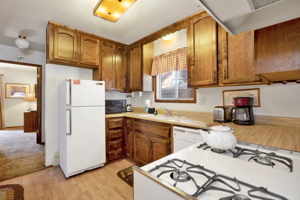 A fully functional kitchen with warm wood cabinetry, modern gas range, and a full-sized refrigerator. Includes all the essentials like a coffee maker and toaster for a convenient home-away-from-home experience.
