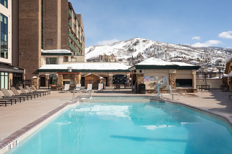 A beautiful mountain resort pool area surrounded by snow-capped peaks and modern accommodations.