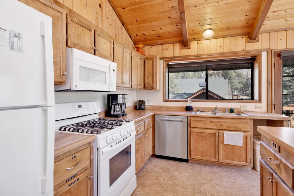 Bright cabin kitchen and dining area with wood ceilings, large island seating, and forest views—ideal for family meals, group cooking, and comfortable mountain getaways.