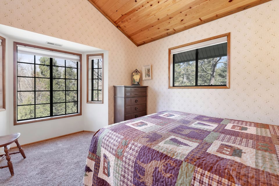 Peaceful cabin bedroom with plush bedding, vaulted wood ceilings, and forest views—ideal for restful nights, cozy mornings, and a relaxing mountain escape.