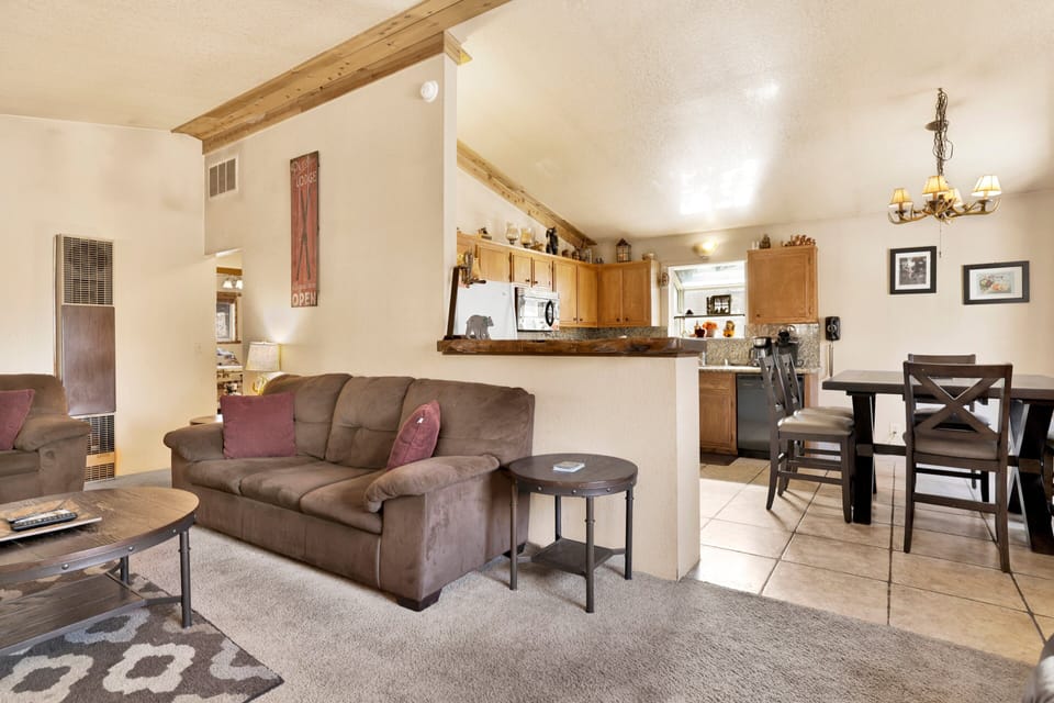 Cozy mountain living room with wood ceilings, stone fireplace, comfy seating, and smart TV—perfect for relaxing evenings, movie nights, and warm cabin vibes after outdoor adventures.