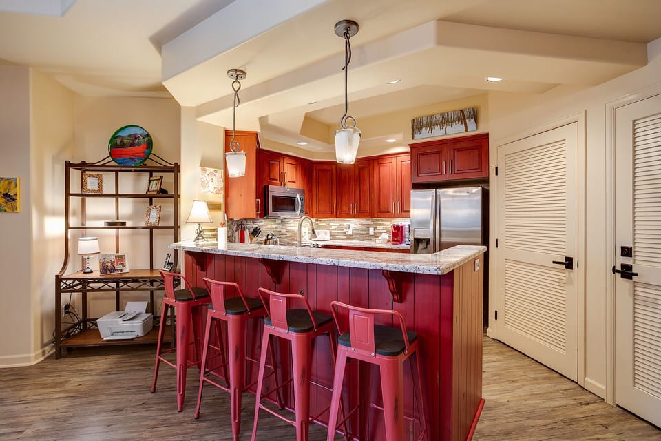 Your fully equipped kitchen awaits with granite counters, stainless appliances, and cheerful red stools for casual dining.