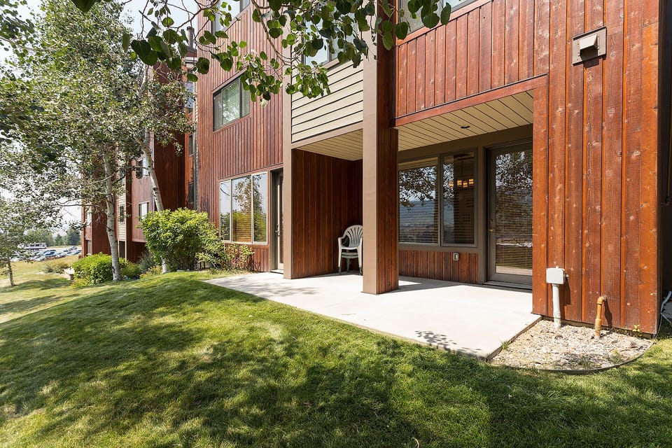 Modern wood-clad building surrounded by mature trees and manicured lawn in a peaceful residential setting.