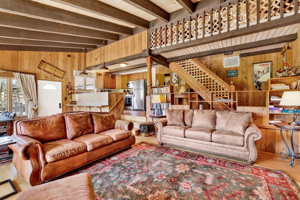Cozy mountain living room with wood ceilings, stone fireplace, comfy seating, and smart TV—perfect for relaxing evenings, movie nights, and warm cabin vibes after outdoor adventures.