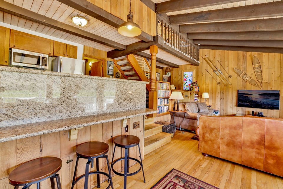 Cozy mountain living room with wood ceilings, stone fireplace, comfy seating, and smart TV—perfect for relaxing evenings, movie nights, and warm cabin vibes after outdoor adventures.