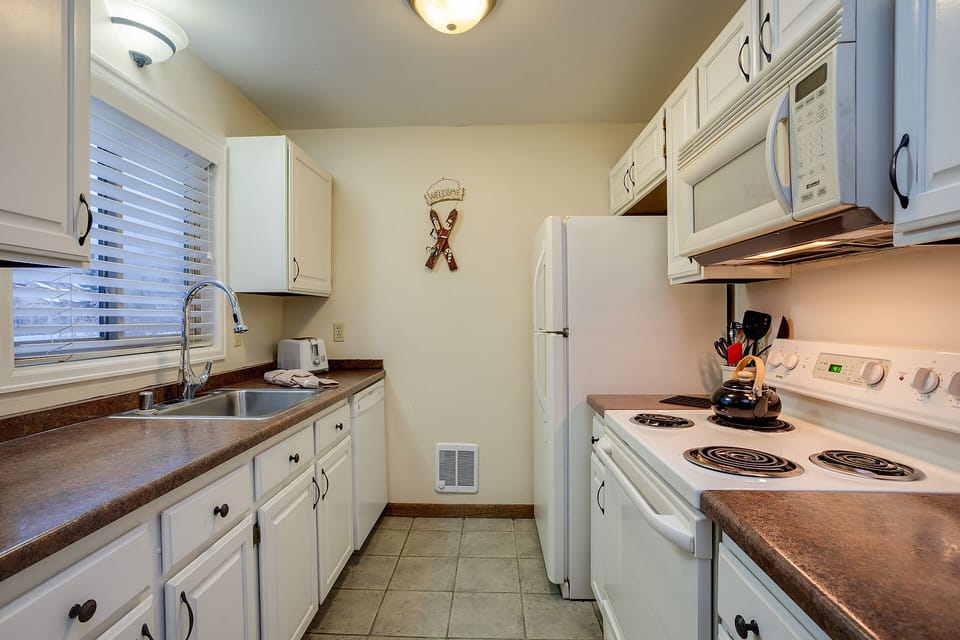 Your fully equipped galley kitchen features everything you need for home-cooked meals, with white appliances and warm countertops creating a welcoming culinary space.