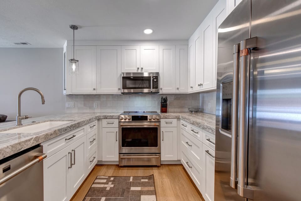 White kitchen cabinets, with grey counters and stainless steel appliances.