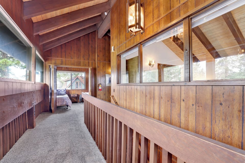 This bright hallway features classic wood-paneled walls and vaulted ceilings. Large windows overlook the living area below, while the plush carpeting leads to the comfortable private bedrooms.