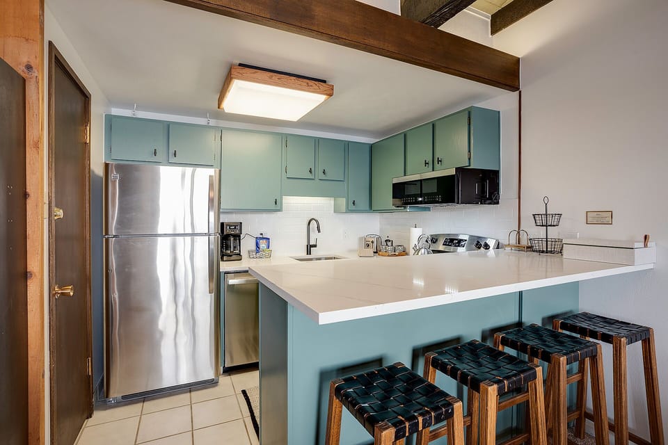 Your kitchen features beautiful exposed beams, sage-green cabinetry, and modern appliances—perfect for preparing meals while soaking in the cozy charm.