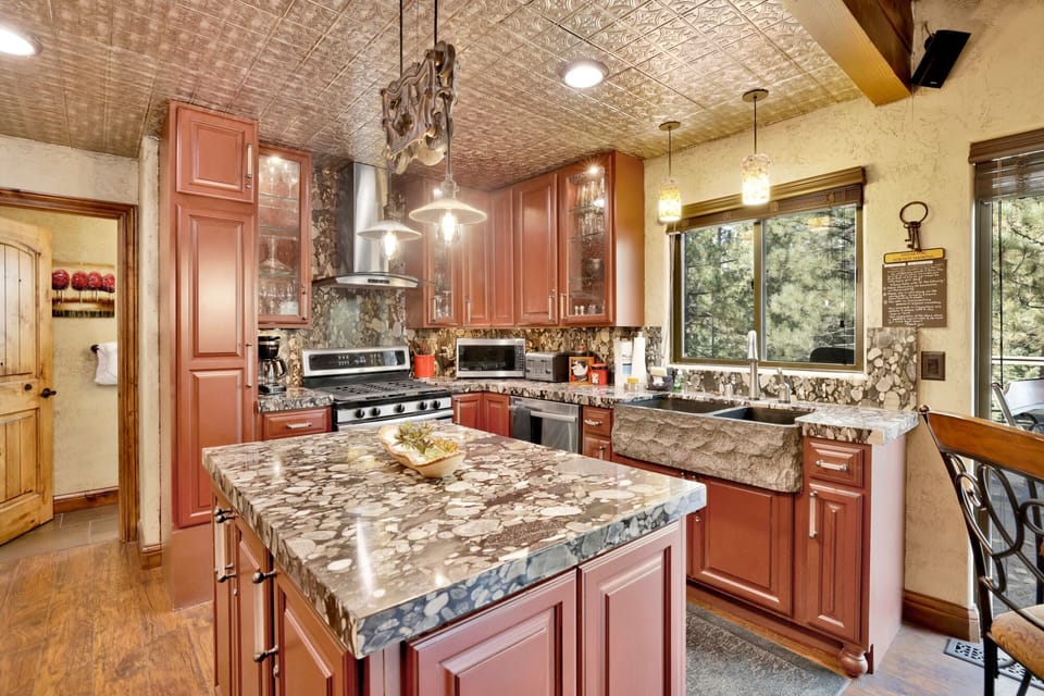 Stunning custom kitchen featuring a large granite island, a rustic farmhouse sink, and elegant tin ceilings.
