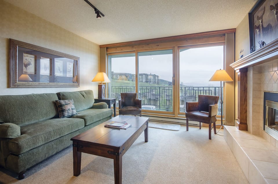 Relax in your cozy living room with a warm fireplace and stunning mountain views through floor-to-ceiling windows.