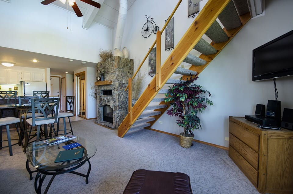 Your mountain retreat features an open living space with stone fireplace, modern amenities, and rustic wooden staircase.