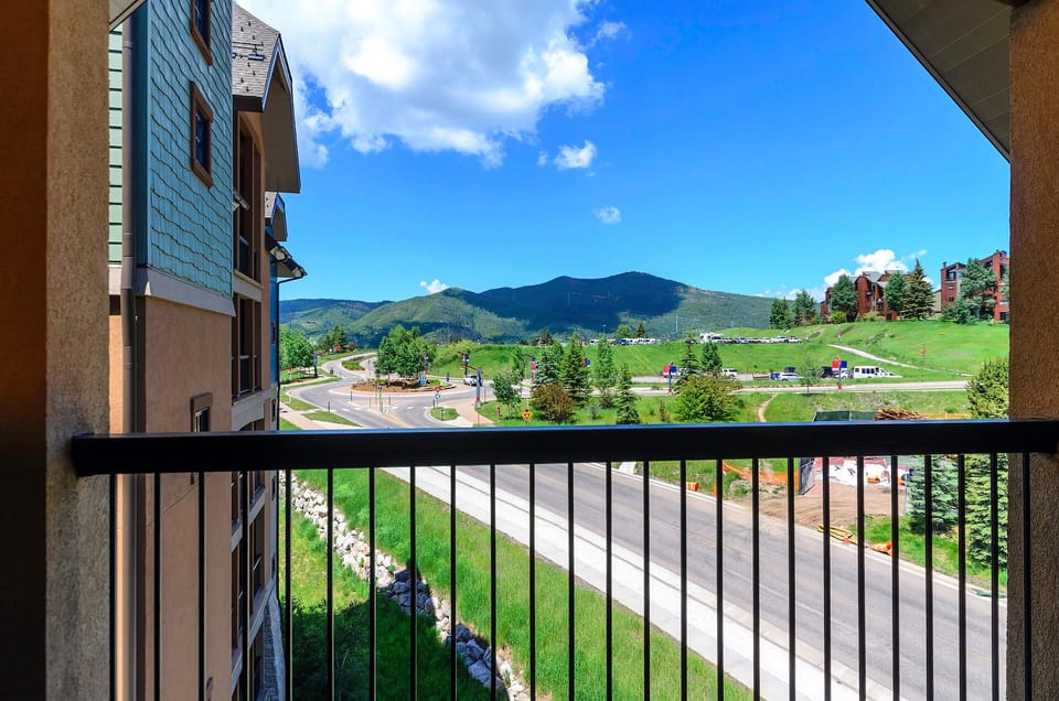 Mountain resort balcony view showcasing green slopes and valley roads beneath dramatic blue skies.