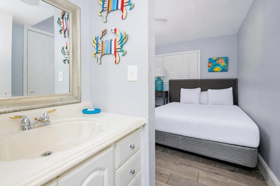 This bathroom features a stylish sink area with a large mirror, leading to a cozy bedroom adorned with colorful decor