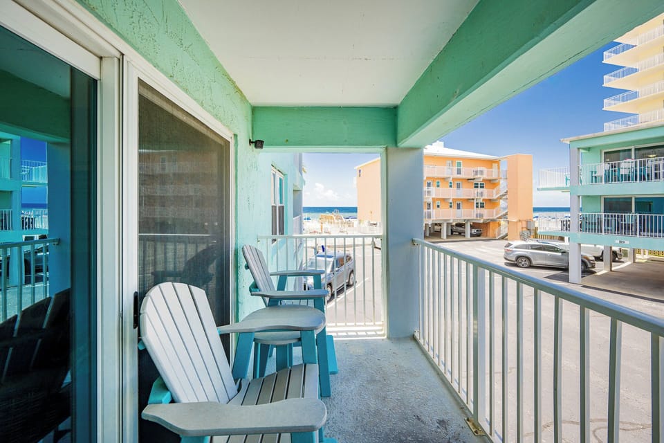 Enjoy a relaxing moment on this balcony with turquoise chairs, offering a view of the beach and nearby vibrant buildings