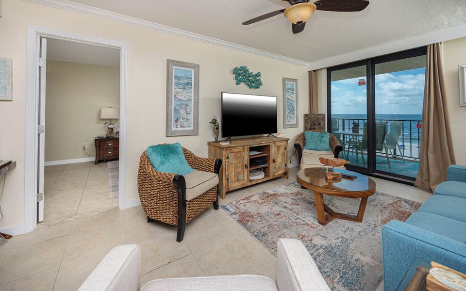This inviting living area features a large TV, cozy seating with a queen sofa-sleeper, and a beautiful view of the beach