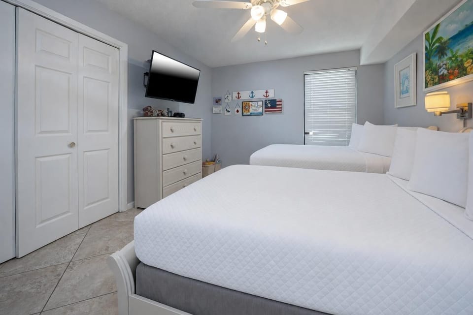This bright guest bedroom features two full beds, a wall-mounted TV, and charming coastal decor