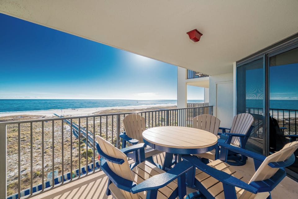Balcony with a round table and adirondack chairs offers a direct view of the beach and the sparkling gulf waters