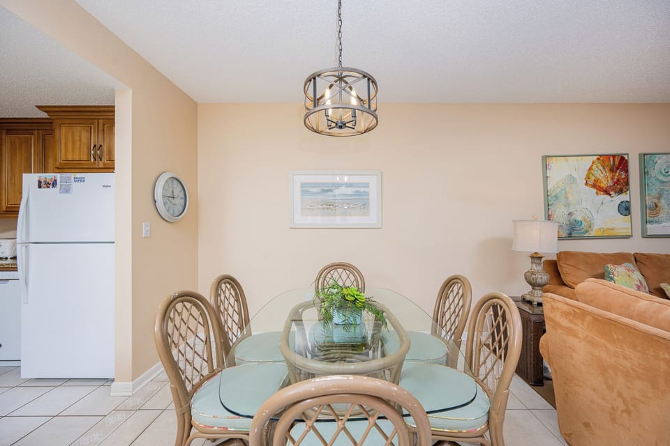 Dining area features a glass table with cushioned chairs, complemented by warm wood cabinetry and colorful art