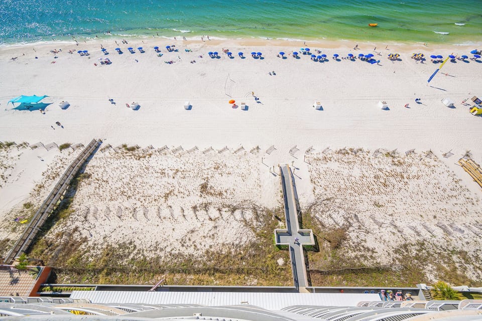 Soft green water laps gently at the shore as colorful umbrellas create a festive scene along the bright sand