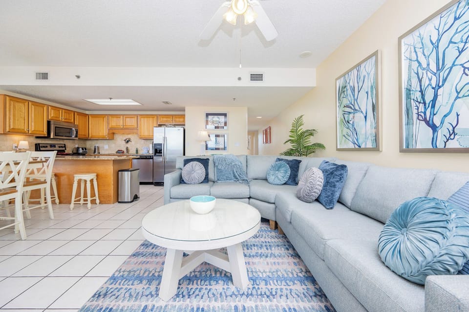 Cozy living area features a spacious sectional sofa with decorative pillows, a glass coffee table, and a breakfast bar nearby