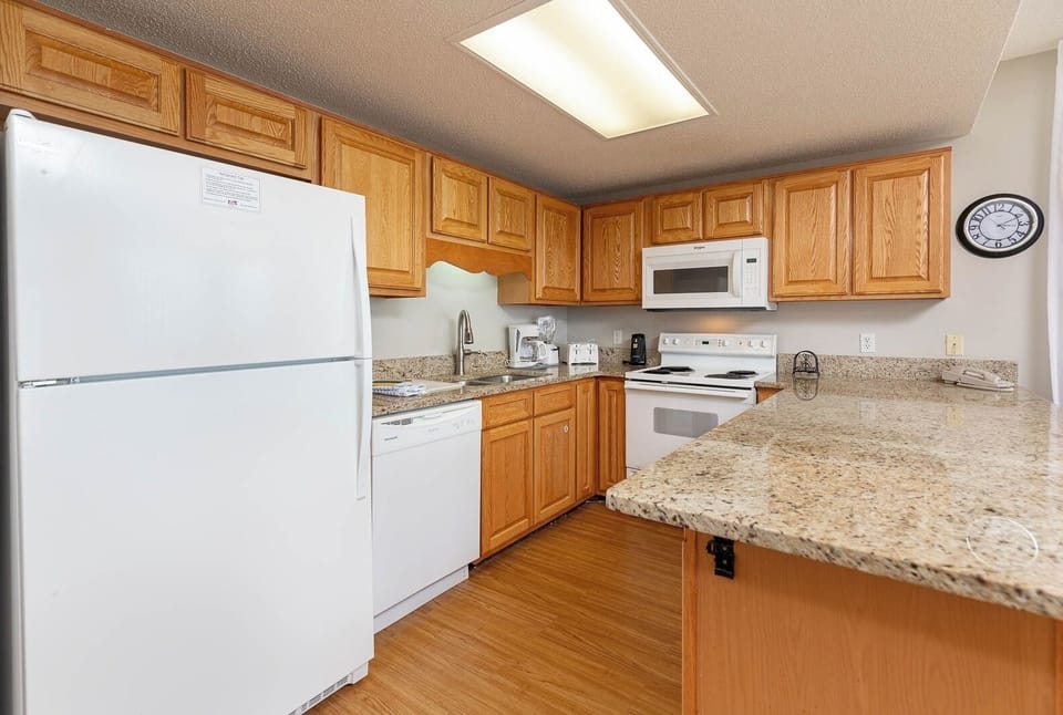 Wooden cabinetry complements the spacious kitchen with granite countertops and white appliances, featuring a breakfast bar