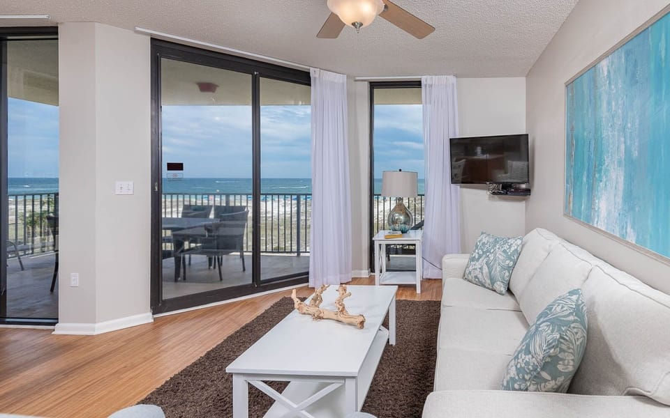 Cozy living area features a light sofa with queen sleeper, a TV, and stunning views of the beach from the balcony
